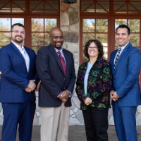 Four award recipients pose and rotate together outside of Alumni House